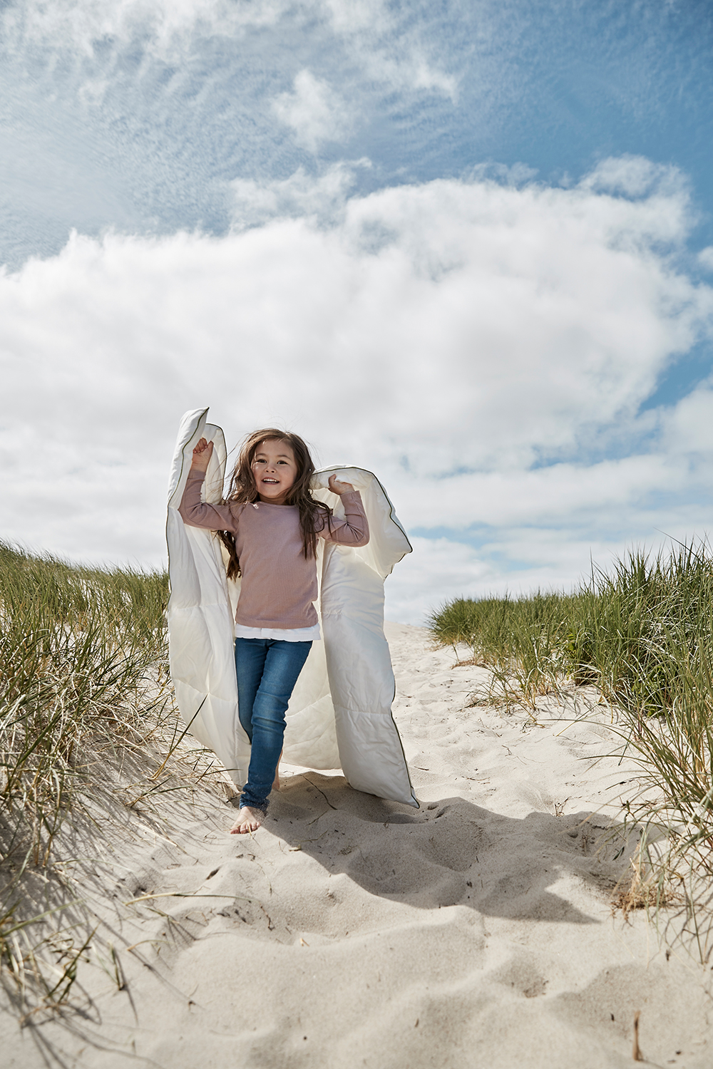 Ett barn bär ett vitt täcke på en stig vid stranden